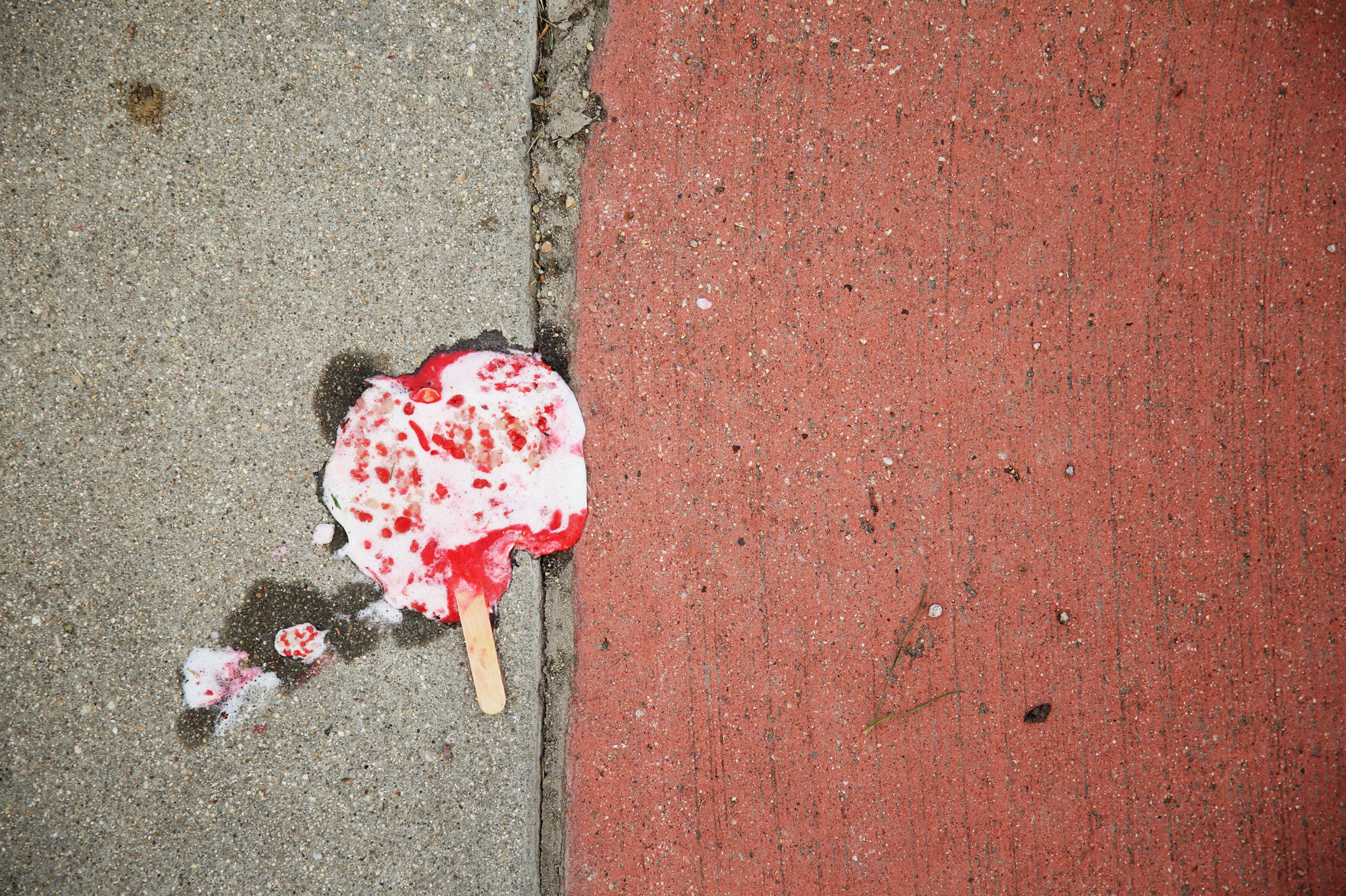 A melted popsicle laid flat on the edge of two sidewalk squares